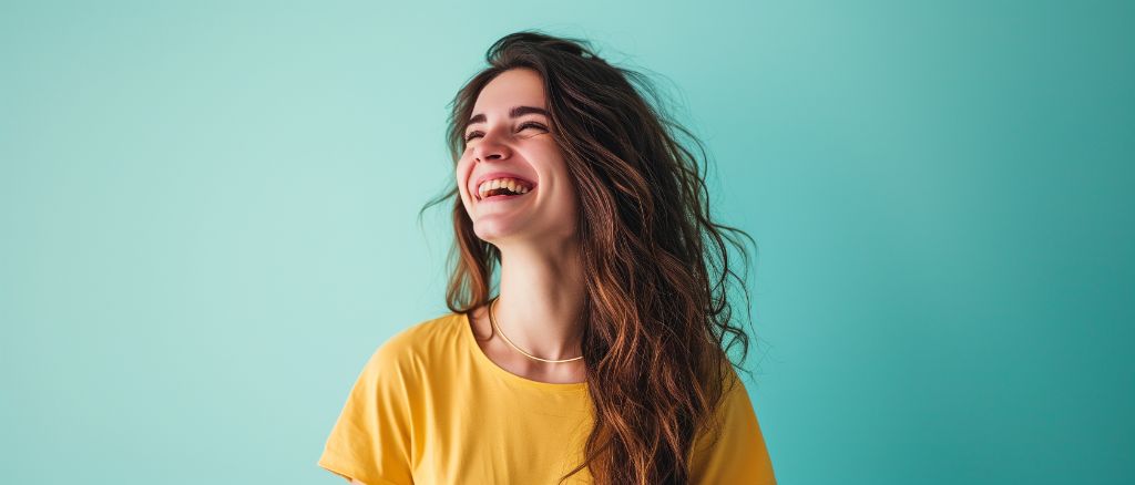 Joyful woman in yellow shirt laughing against a teal background