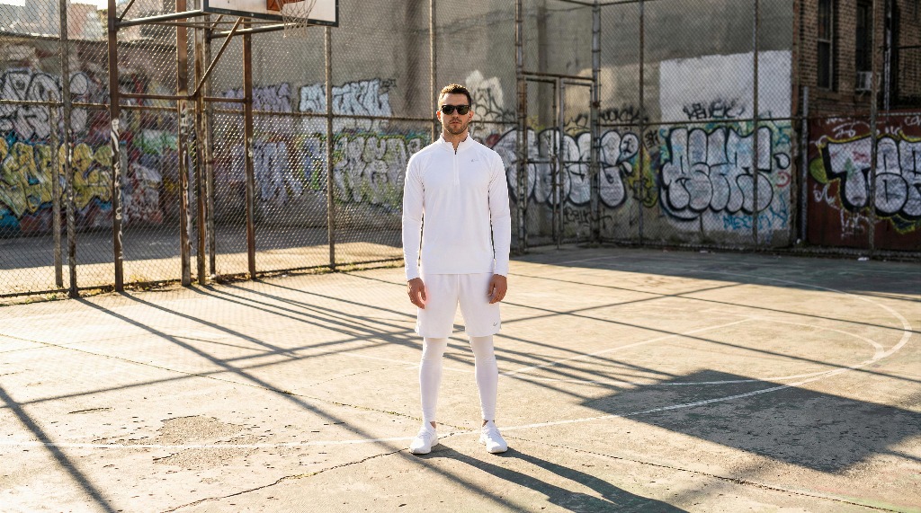 Man in white outfit stands on graffiti-covered basketball court.