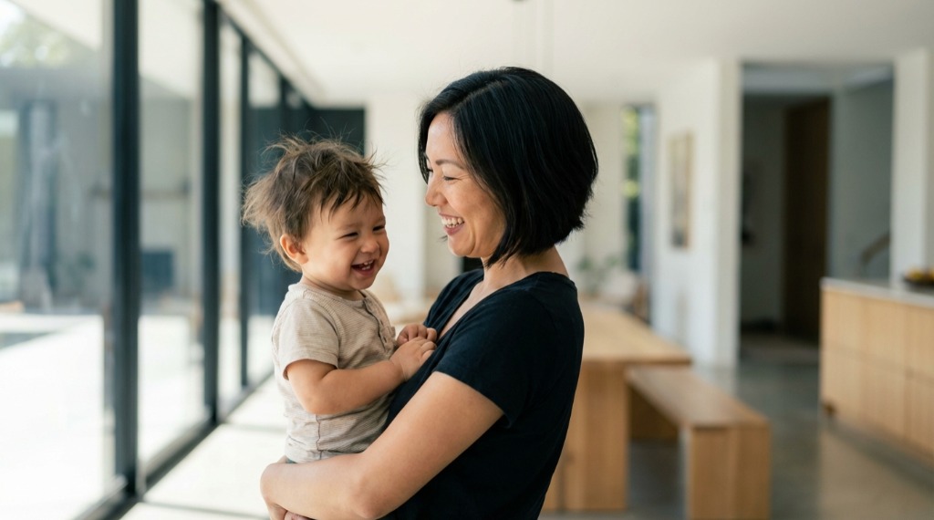 Smiling woman holding a laughing toddler in a bright room.