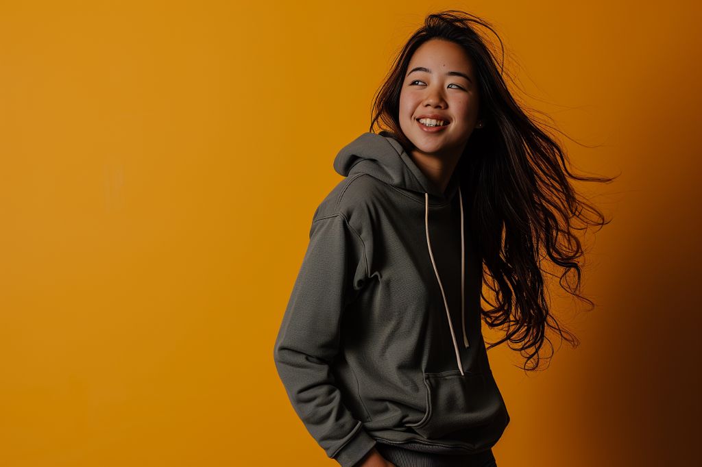 Smiling young woman in a gray hoodie against a yellow background