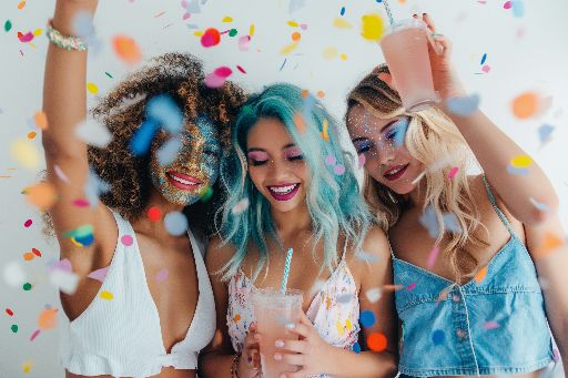 Three joyful women celebrating with confetti and drinks