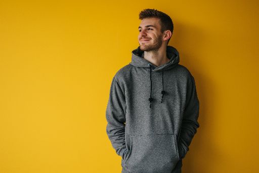 Smiling young man in a hoodie against a yellow background