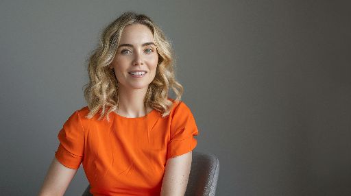 Woman in orange dress sitting with a confident smile