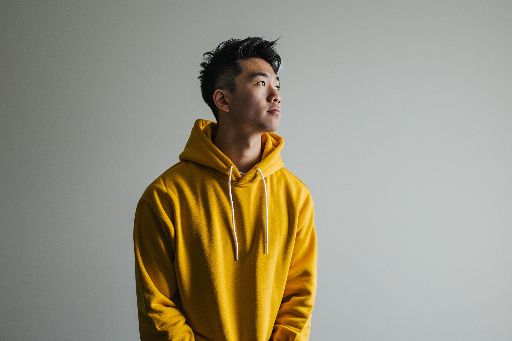 Man in yellow hoodie looking up thoughtfully against a neutral background