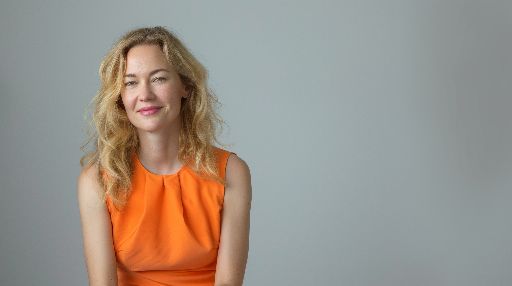 Woman in orange dress smiling against a grey background