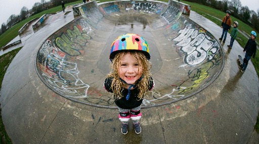 Young girl with colorful helmet at a graffiti-covered skatepark.