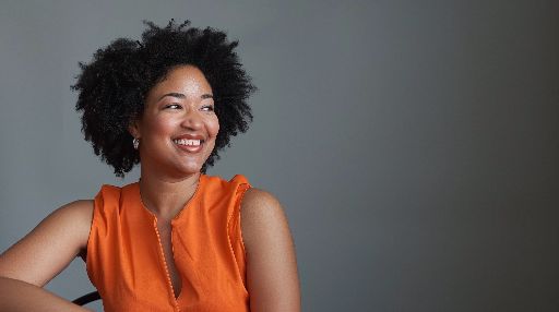 Smiling woman with natural hair in orange blouse against grey background