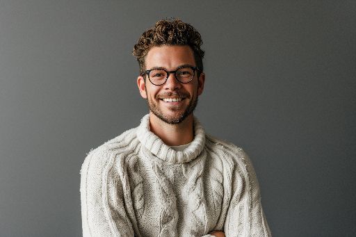 Smiling man with glasses wearing a white sweater against a grey background