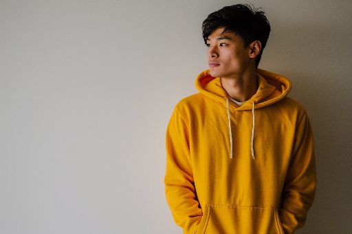 Young man in yellow hoodie looking thoughtful against a neutral background