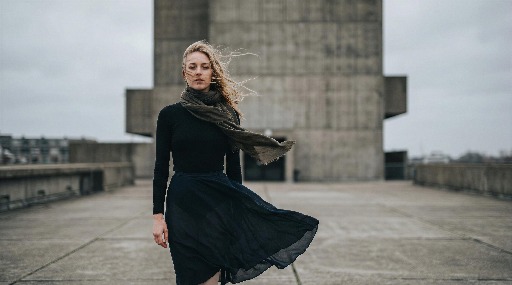 Woman in black dress standing on a concrete rooftop.