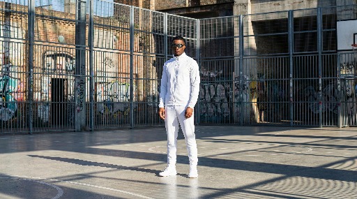 Young man in white outfit stands on urban basketball court.