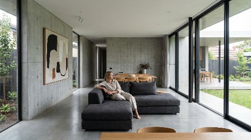 Woman sitting on a sofa in a modern living room with large windows.
