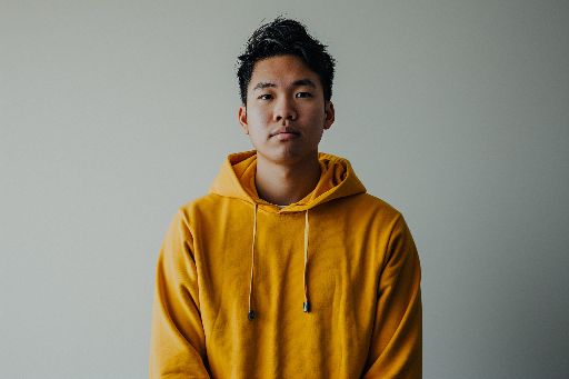 Young man in yellow hoodie standing against a neutral background