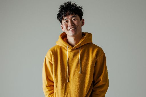 Cheerful young man in a yellow hoodie smiling against a grey background