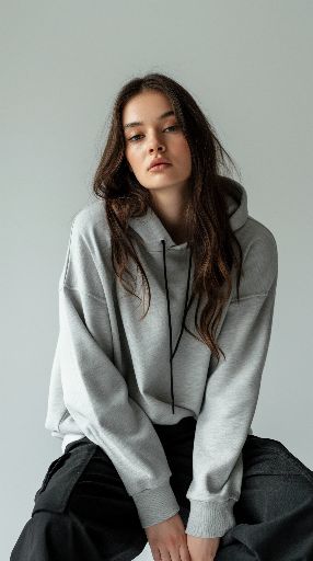 Young woman in a casual grey hoodie and black pants posing