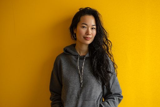 Confident young woman in a gray hoodie against a yellow wall